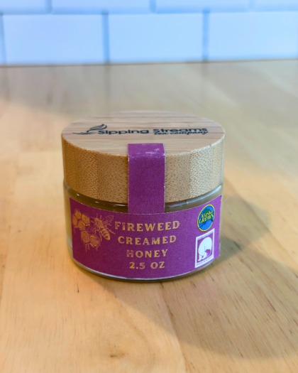A 2.5 oz round glass jar of Fireweed Creamed Honey with a bamboo lid. The purple label has gold text and honeycomb graphics, emphasizing its Alaska-grown origin and creamy texture made from fireweed nectar.