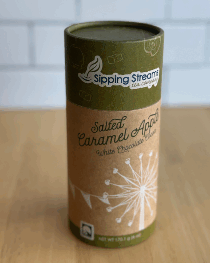 An elegant 8 oz canister of Salted Caramel Apple Hot Chocolate from Sipping Streams Tea Company, filled with a smooth cocoa mix infused with caramel sweetness, apple brightness, and a hint of salt.