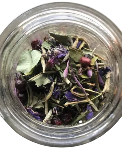 An overhead view of a clear glass jar filled with loose-leaf Arctic Bliss Fireweed Tea. The blend includes green leaves, purple petals, and red lingonberries, showcasing its wild-foraged Alaskan ingredients. A clean, vibrant mix ideal for herbal tea lovers and eco-conscious shoppers.