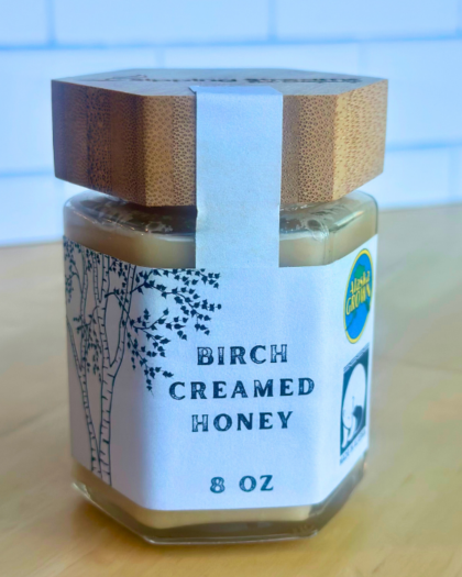 An 8 oz jar of Sipping Streams Tea Company's Birch Creamed Honey, designed with a natural aesthetic featuring a birch tree illustration and a bamboo-style lid. The honey is smooth, rich, and naturally sweet, crafted with high-quality Alaskan ingredients.