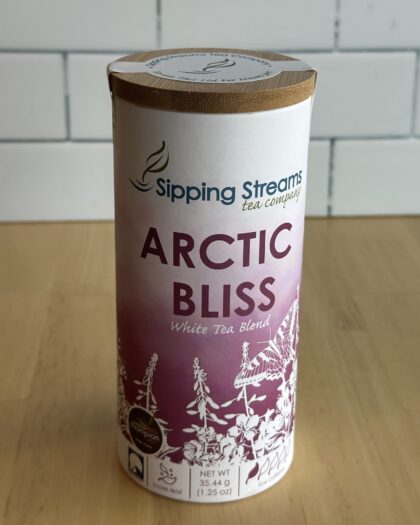 A tall tin of Sipping Streams Tea Company's Arctic Bliss White Tea Blend. The label showcases bright fireweed flowers and mentions the use of 100% wild Alaskan-grown fireweed and lingonberry. The tin contains 1.25 oz of loose-leaf tea