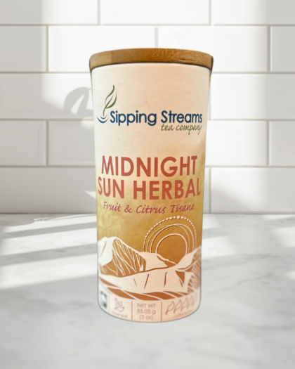 A tall tin of Sipping Streams Tea Company's Midnight Sun Herbal Blend. The label displays dried fruit and citrus ingredients, indicating it is a caffeine-free, fruit and citrus loose tisane. The tin contains 3 oz of loose-leaf tea