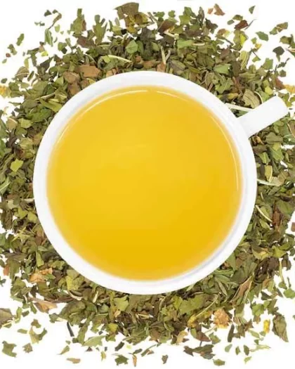 A top-down view of a white cup filled with golden herbal tea, encircled by scattered loose peppermint leaves. The image emphasizes the freshness, purity, and soothing nature of Sipping Streams’ Organic Peppermint loose-leaf tea.