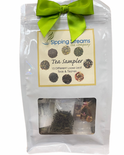 Gift-ready Tea Sampler pack from Sipping Streams Tea Company, showcasing 15 individually packed loose leaf tea and tisane samples in a white pouch with a clear window and green ribbon. Sold in a case of 12.