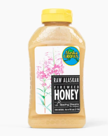 A 1 lb bottle of Raw Alaskan Fireweed Honey from Sipping Streams Tea Company. The clear plastic container has a yellow cap, a fireweed flower illustration, and an 'Alaska Grown' certification, showcasing the natural golden honey inside.