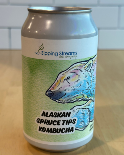 A 12 oz can of Sipping Streams Tea Company's Alaskan Spruce Tips Kombucha, designed with a green label featuring a polar bear illustration. This probiotic-rich kombucha is made with locally harvested Alaskan spruce tips, delivering a unique and refreshing herbal flavor packed with health benefits.