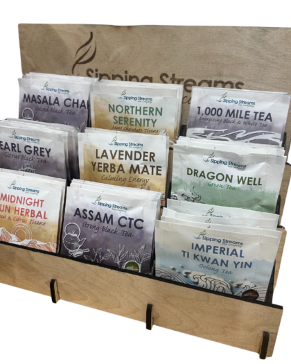 A wooden stand-up tea display rack holding nine flavors of individually wrapped pyramid tea sachets from Sipping Streams Tea Company.