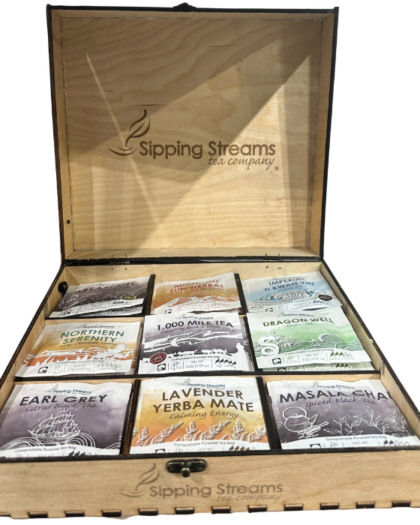 Open wooden tea sachet display box with Sipping Streams logo, holding nine individually wrapped pyramid tea sachets arranged neatly inside.